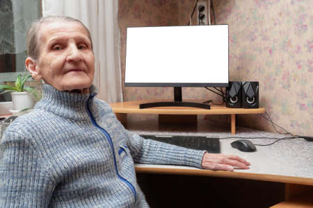A modern grandmother of 70 years is sitting at the computer. An elderly woman proudly smiles against the background of a white PC screen. The concept of Internet communication, winning the game.の写真素材
