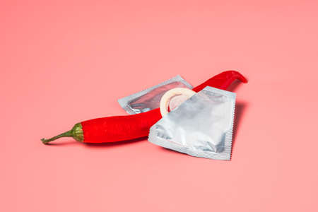 One red hot chili pepper lies in condoms on a pink background. The concept of protection against sexually transmitted diseases.の写真素材