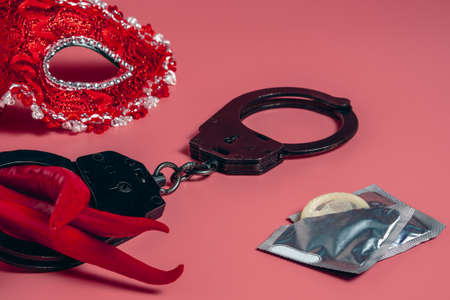 Traditional Venetian red mask on a pink background. Red hot Chili pepper in police handcuffs next to condoms. The concept of seduction, sex and love. Valentine's day.の写真素材