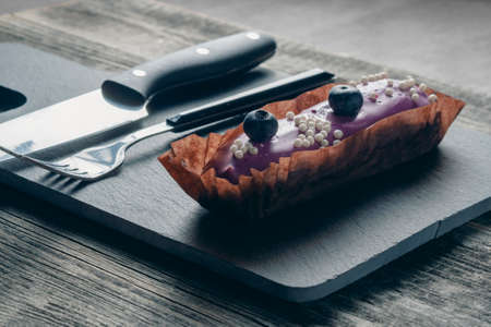Dessert covered with purple glaze on a slate black board with a serving fork and knife. Decorated...