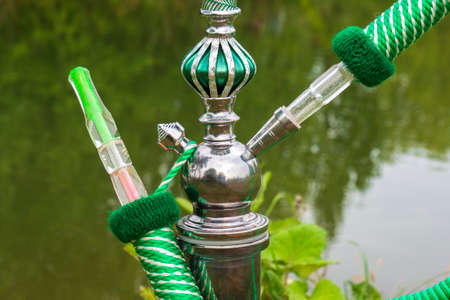 A green hookah in close-up stands on the bank of a river in the forest. The concept of outdoor...