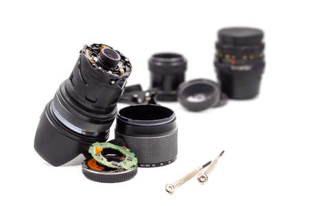 Broken and smashed camera lens lies with screwdrivers on the table in the workshop. Damaged modern photo lens with an electronic filling and a bayonet (lens mount) on a white background.の写真素材