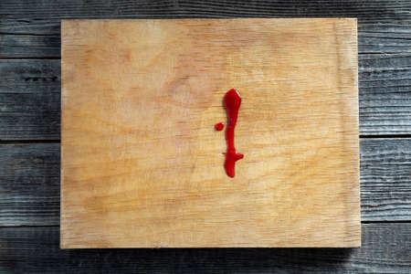 Drops of blood or red juice on an old dirty kitchen cutting board close up. The concept of domestic trauma.の写真素材