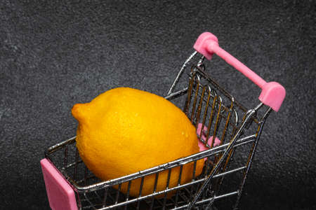 Washed yellow lemon with water drops in a shopping cart on a black background. The concept of buying vegetables and fruits.の写真素材