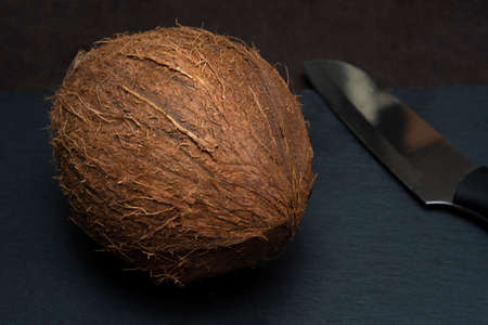 Brown coconut with serving knife on a slate blackboard. The concept how to open a coco nut.