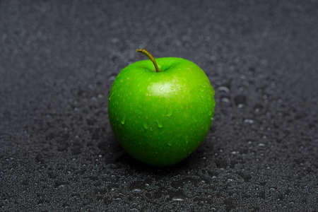 Washed green apple with water drops on a black background close up.の写真素材