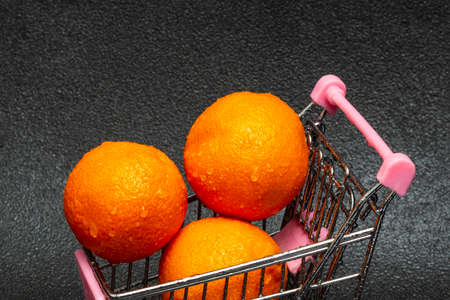 Washed tangerines with water drops in a shopping cart on a black background. The concept of Christmas foodの写真素材