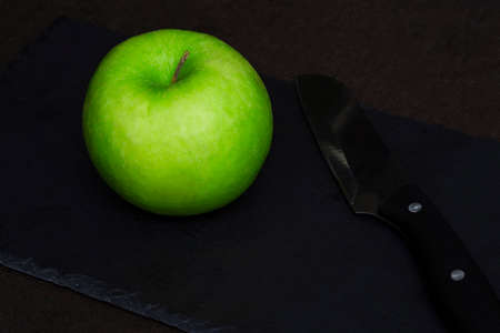 A green apple next to a serving knife on a black slate board. The concept of a healthy food or diet.の写真素材