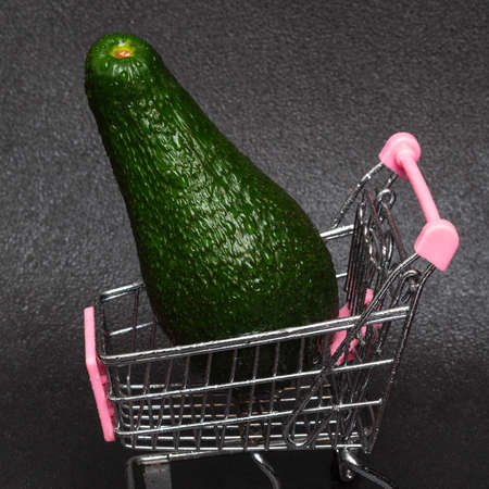 Washed green avocado with water drops in a shopping cart on a black background. The concept of diet and eating healthy.の写真素材