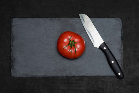 Red tomato with a serving knife on a slate black board. The concept of healthy food, diet.の写真素材