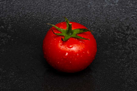 Washed red tomato with green foliage and drops of water on a black background close up.の写真素材