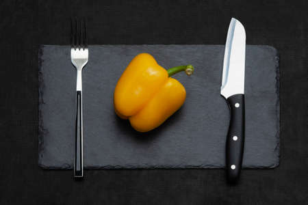 Yellow bell pepper with fork and knife black slate board. The concept of diet, food preparation.の写真素材