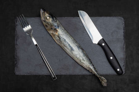 Frozen fish with a serving fork and knife on a slate black cutting board. The concept of a seafood diet.の写真素材