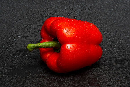 Washed red bell pepper with water drops on a black background.の写真素材