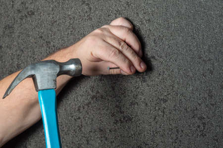 Man hammer a nail into a black wallpaper wall. Close-up of hands with a construction tool. DIY concept, husband for an hour.の写真素材
