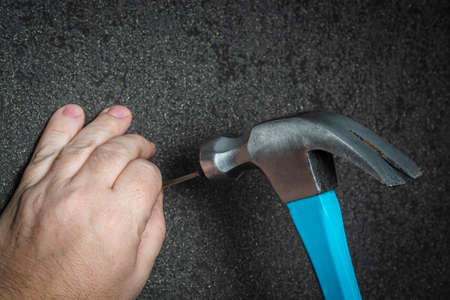 Man hammers a nail into a black wallpaper wall. Close-up of hands with a construction tool. DIY concept, husband for an hour.の写真素材