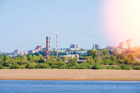 View of the urban industrial area across the river. Summer green country landscape with factory...