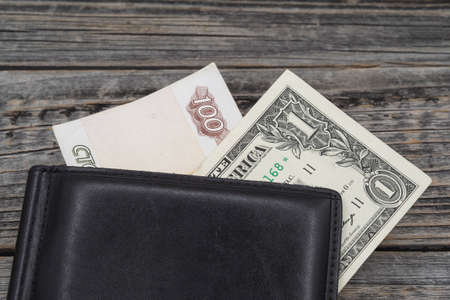 Two money bills in a black wallet on a wooden table background. One American dollar and one hundred...