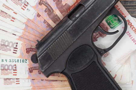 Many five thousand Russian money banknotes lie in a fan on a wooden table background with a black police pistol. The concept of economic crime, theft or robbery.の写真素材