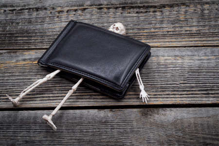 Human skeleton, bones and skull in a closed black leather wallet on a gray old wooden table...