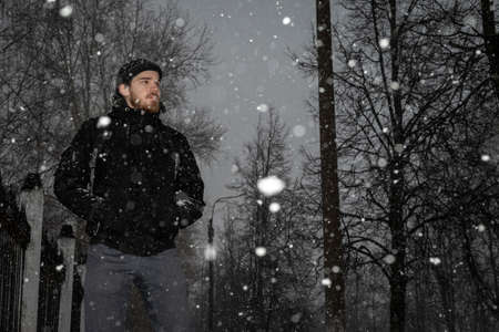 A lonely sad man in a black knitted hat and a black jacket looks into the distance against the...