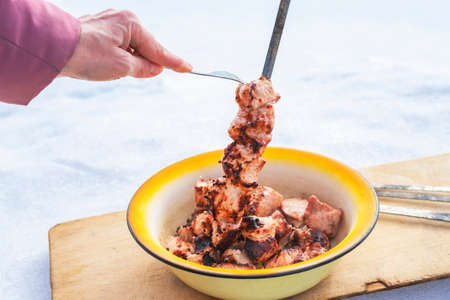 Woman removes meat from a skewer with a fork into a plate on a wooden cutting board against the...