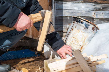 A man is chopping wood splinters with an ax to kindle a fire.