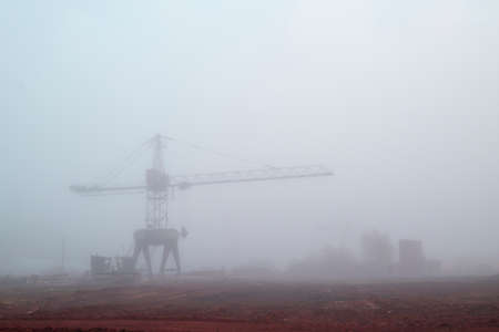 Mystical landscape of a sawmill construction crane against the background of morning fog. Pollution and smog on the construction site. Concept of abandoned manufactured factory.の写真素材