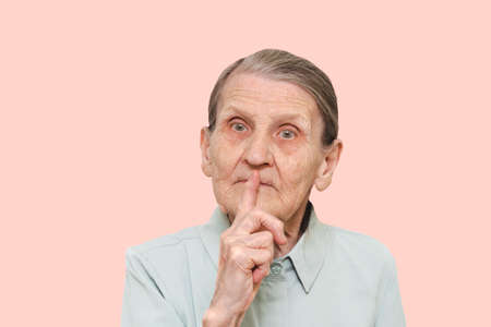 An elderly woman uses sign language. Portrait of a dumb old lady with a finger on her lips. The...