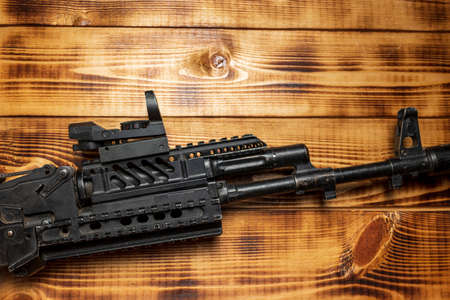 Automatic assault rifle on a wooden table background close-up. Modern black assault gun.
