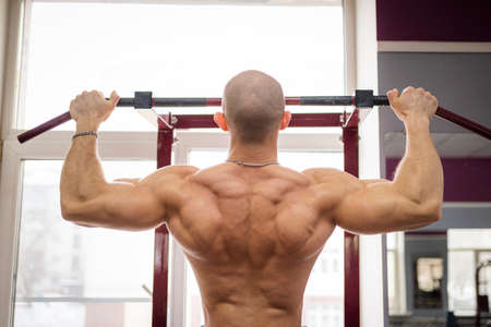 Man pulls himself up on a crossbar in the gym. Bodybuilder trains with a horizontal bar.