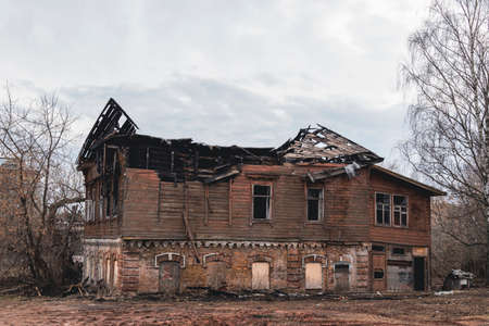 An old historical wooden burnt out house against a gray sky. An abandoned building set on fire.