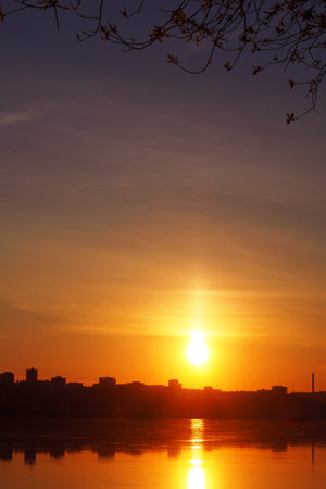 The river against the silhouette of the town in the rays of the setting sun. A pillar of sun light in a dramatic sky.の写真素材