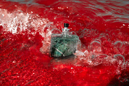 Toilet water in red sea waves. A turquoise glass bottle of perfume against the background of a river and water splashes.の写真素材