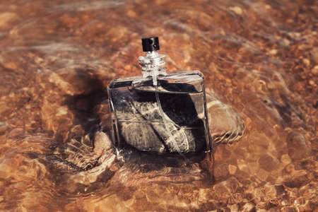 Men's toilet water in sea waves. A glass bottle of perfume against the background of a river and water splashes. The concept of masculinity and freshness fragrance.の写真素材