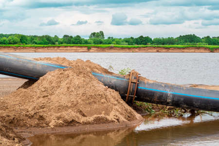 Modern rubber pipe next to the water by the river. The concept of environmental pollution.