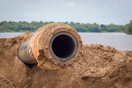 Modern rubber pipe next to the water by the river. The concept of environmental pollution.の写真素材