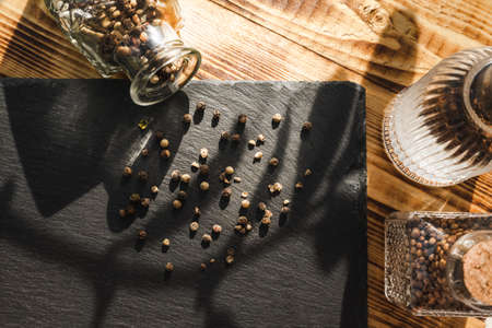 Mixture of peppers spilled from a glass bottle for storing spices on a black slate cutting board on...