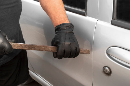 A man holds a tire iron in his hands with black leather gloves and opens the automobile door....