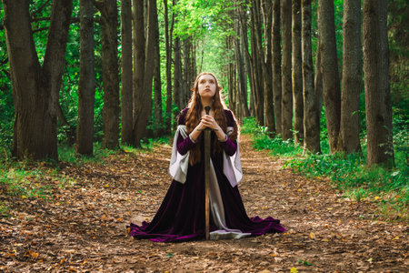An elven girl driver with long red hair in a purple dress in the forest poses sitting with a...