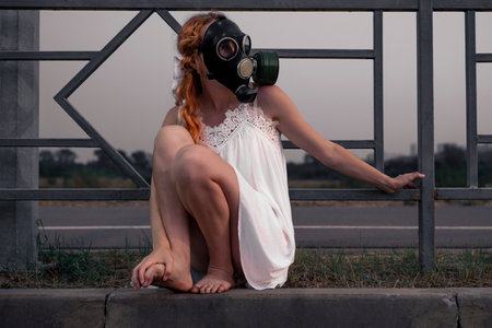 A barefoot woman in a white dress wearing a gas mask stands in the middle of a road in the city. The concept of nuclear threat.の写真素材