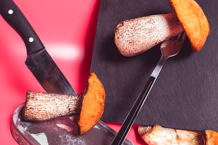 Mushroom on a cutting slate board with a fork and knife on a pink background. The concept of...