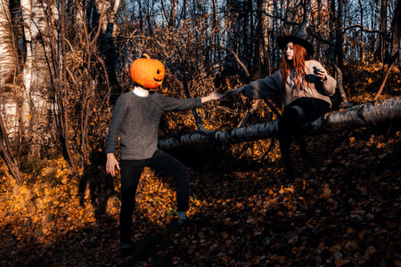Witch woman sits on a birch tree and orders a man with a jack lantern on his head.の写真素材