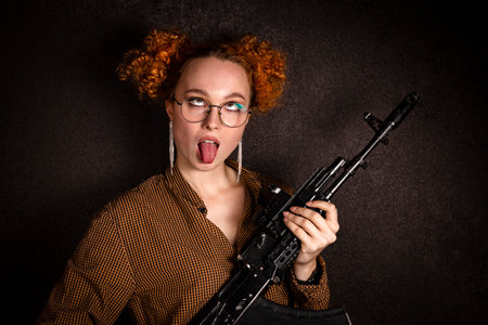 Portrait of a cheerful red haired civilian clothes woman with an assault rifle in her hands on a...