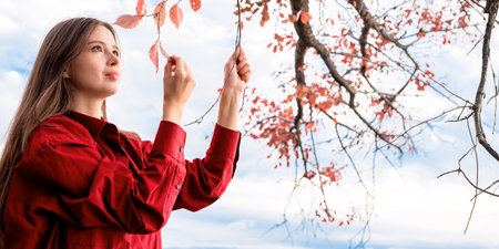 Portrait of a woman in a red men's shirt touching and holding in her hand a tree branch with red...