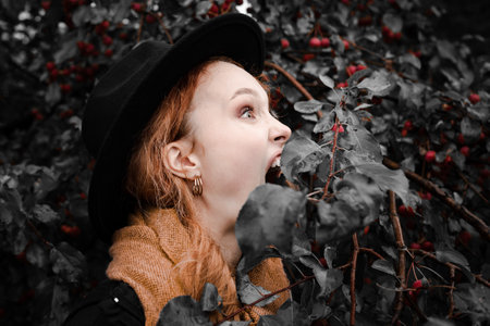 Portrait of a woman with an open mouth biting a small red apple on an apple tree branch.