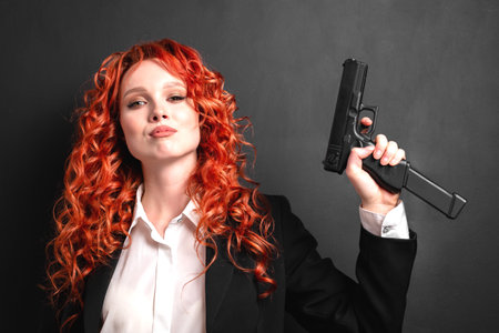 Portrait of a young red-haired woman armed with a pistol in a business suit. The concept of the...