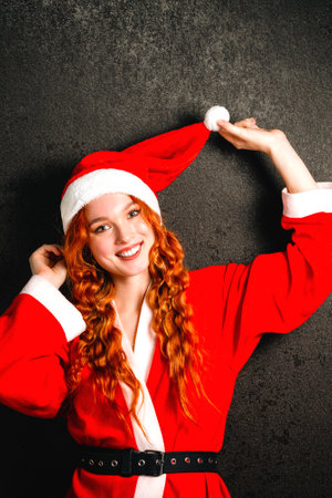 A happy young girl in a Santa Claus costume smiles on a black background. Portrait of a red-haired woman in a red cap laughing on a dark background. The concept of Christmas and New Year.の写真素材