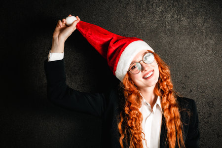 Portrait of a red-haired business woman in a suit with a red Christmas hat.の写真素材
