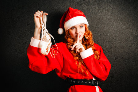 A smiling red-haired woman in a hat and Santa Claus costume undresses and holds beige underpants in her hands. The concept of seduction and sexuality.の写真素材
